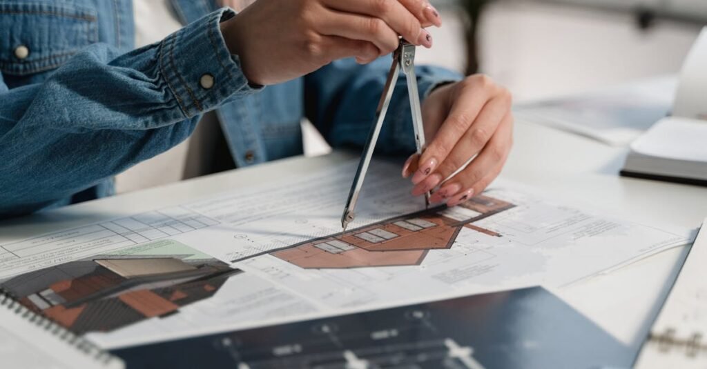 A creative professional using a compass on blueprints at an office desk.